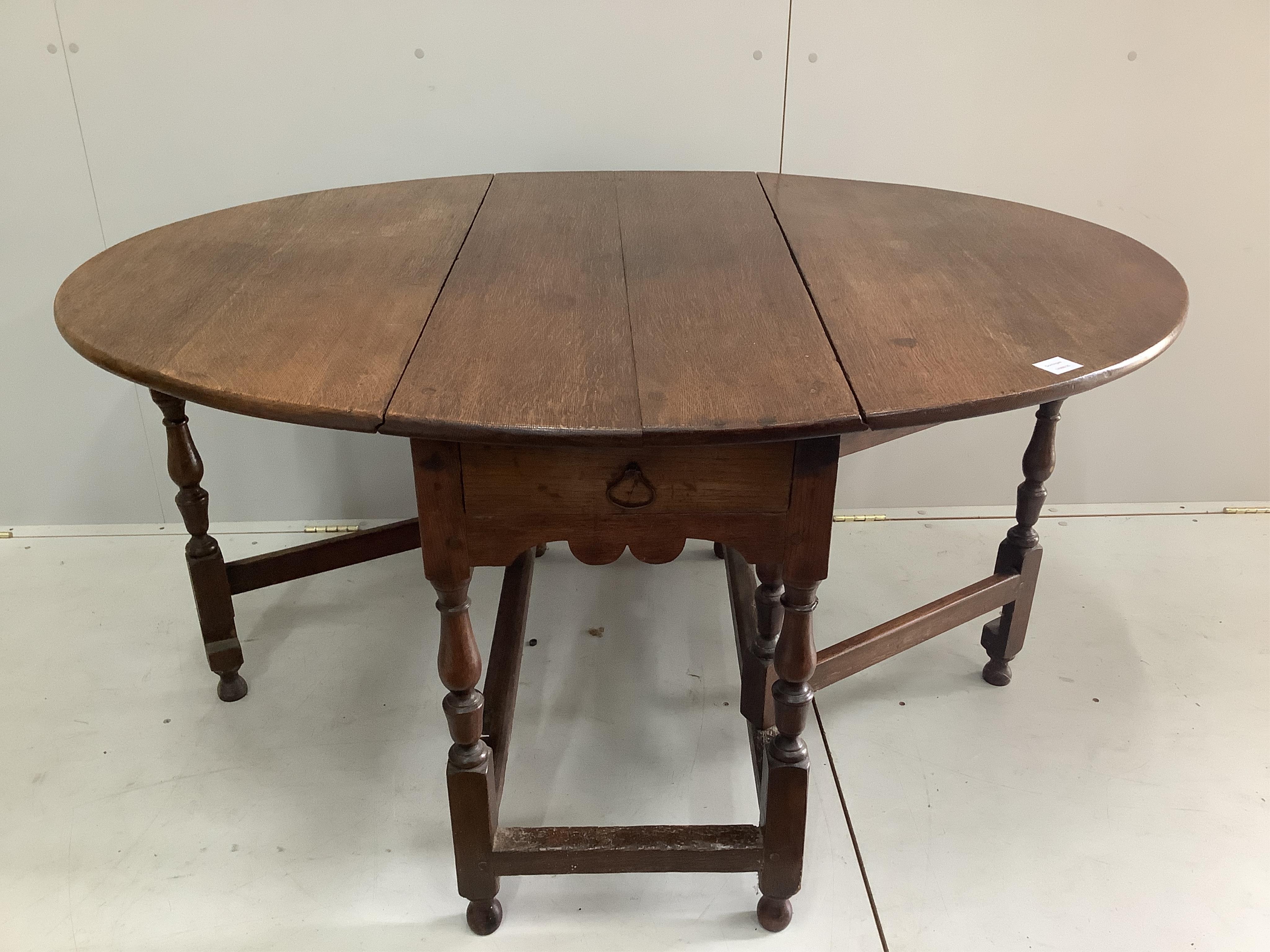 An early 18th century oak oval topped gateleg dining table, fitted with a drawer, width 104cm, depth 47cm, height 73cm. Condition - fair